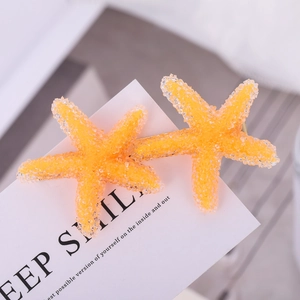 Close-up of two bright orange starfish hair clips with glitter on white card