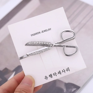 Pince à cheveux ciseaux argentée avec strass scintillants sur une carte de bijoux