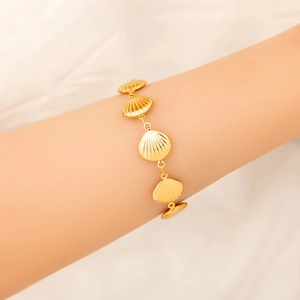 Detail of 18K gold shell bracelet with intricate textured sea motifs on white fabric
