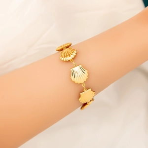 Detail view of 18K gold plated ocean-style shell bracelet worn on a female wrist