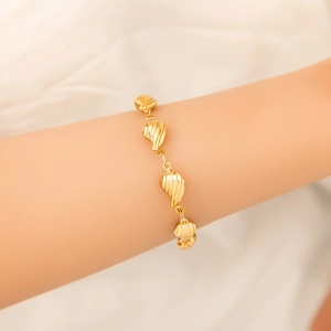 Detailed view of an 18K gold shell bracelet with textured charms on a person's wrist