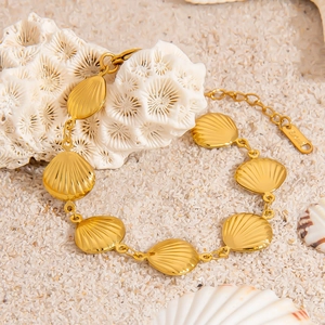 Detail of 18K gold plated stainless steel shell bracelet on white sand with coral decor