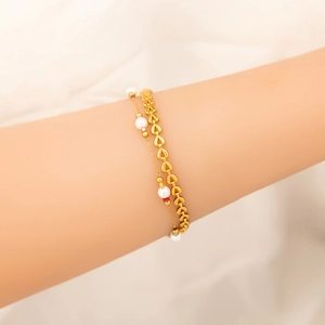 Dettaglio di un bracciale a doppio strato dorato con perline a cuore e perle bianche