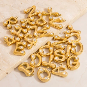 Polished 18K gold bubble letter pendants with sparkling cubic zirconia on a stone surface