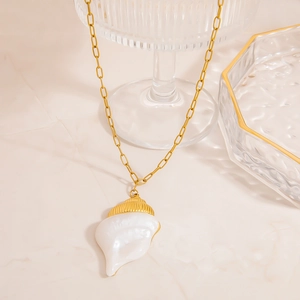 Detail of gold paperclip chain necklace with a white conch shell pendant on glass