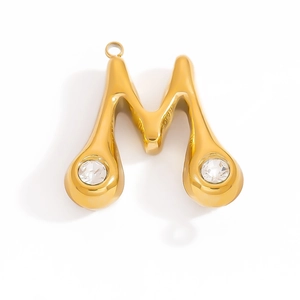 Macro detail of gold-plated letter M pendant with cubic zirconia stones on white background