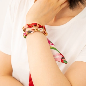 Detail eines roten Seidenschals, geflochten mit goldenem Edelstahlkettenarmband am Handgelenk