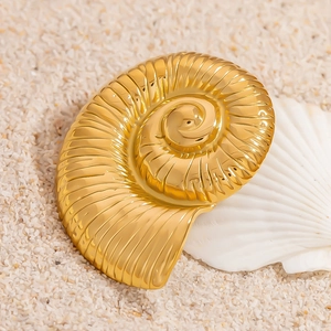 18K gold nautilus shell brooch with spiral texture on a sandy beach background