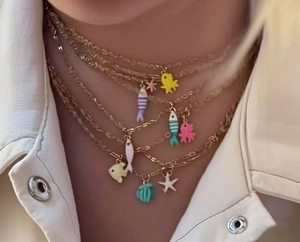 Macro detail of layered gold necklaces with colorful enamel sea fish and starfish charms