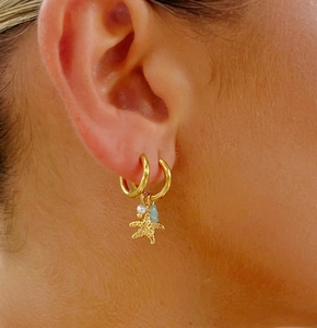 Detailed close-up of a gold starfish earring with pearl and blue bead on model ear
