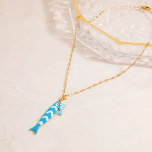 Detail of gold tropical fish necklace with blue enamel on a marble surface background