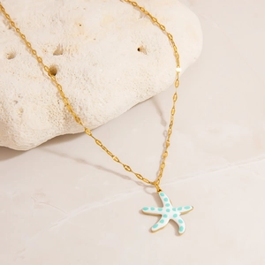 Detailed macro view of a gold starfish pendant with white and teal enamel on a stone