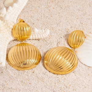 Goldene Titanstahl-Ohrringe mit gerippter Textur auf Strandsand mit Muscheln liegend