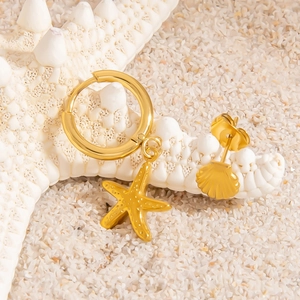 Detail of gold starfish and seashell charms on white sand for marine-inspired ocean jewelry