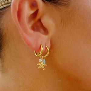 Gold stainless steel starfish hoop earrings with pearl and blue stone on model ear