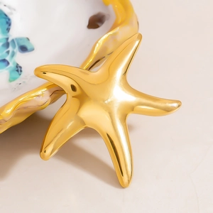 Polished 18K gold stainless steel star ring displayed on a coastal ceramic plate