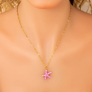 Detailed close-up of a pink starfish pendant with white polka dots on a gold chain