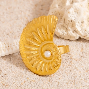 Golden nautilus shell ring with a white pearl on sand and white coral beach background