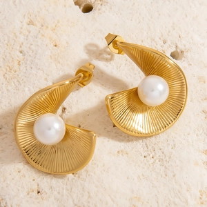 Detailed close-up of gold shell-shaped pearl stud earrings on a textured stone
