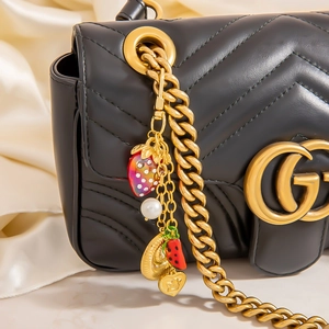 Close-up of black quilted leather bag with gold chain and cherry pearl charms