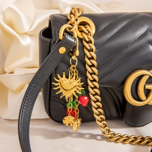 Close-up of black quilted leather shoulder bag with gold G-logo and strawberry charm
