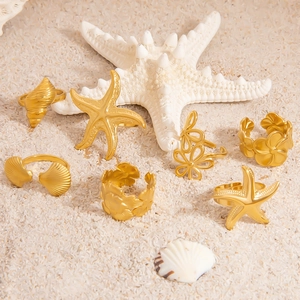 Set di anelli dorati in acciaio inossidabile con stelle marine e conchiglie sulla sabbia