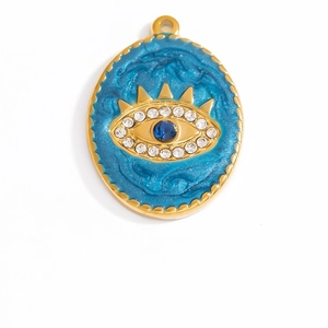Macro detail of 18K gold evil eye oval pendant with blue enamel and crystal accents
