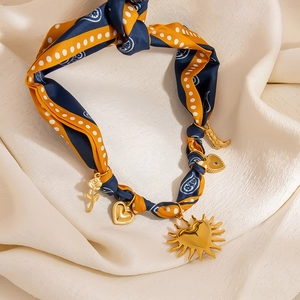 Elegante Halskette mit blauem Seidenband und goldenen Anhängern auf beigem Hintergrund