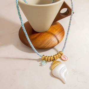 Detail of colorful braided cord necklace with large seashell and multi-charm pendants