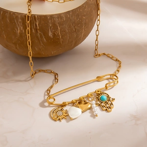 18K gold-plated paperclip necklace with celestial Hamsa and pearl charms on brown coconut