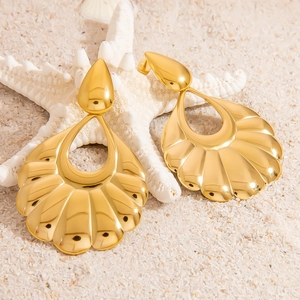 Detalle macro de pendientes de concha dorados sobre fondo de arena de playa y estrella de mar