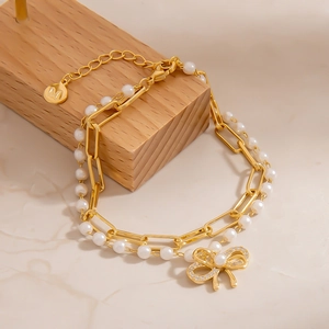 Detail eines zweischichtigen Armbands mit Perlen, Goldkette und Glitzer-Schleife
