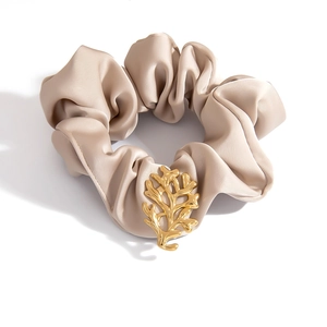 Haargummi aus champagnerfarbenem Satin mit goldenem Korallenakzent auf weißem Hintergrund