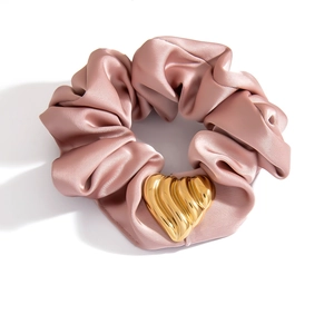 Detail eines rosa Satin-Haargummis mit einem strukturierten goldenen Herz-Metallanhänger