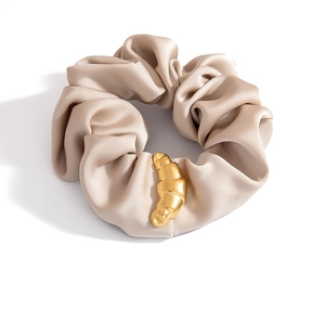 Detail eines champagnerfarbenen Satin-Scrunchie mit goldenem Croissant-Anhänger aus Metall