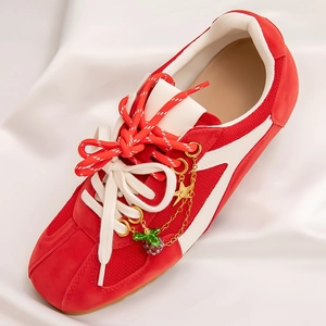 Detail of red mesh sneaker featuring decorative gold star and berry charms on laces