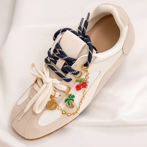 Detail of cream sneakers with creative charms like golden coins and cherries on satin fabric
