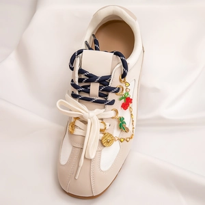 Close-up of beach-style gold shoe charms on a beige sneaker with palm and cherry motifs