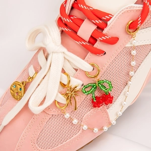 Close-up of pink sneaker charms with gold pendants, cherry beads, and faux pearl chain