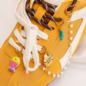 Close-up of beach style charms and pearl chain set on yellow mesh sneakers