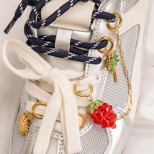 Detail of gold charms with strawberry and palm tree pendants on a silver mesh sneaker