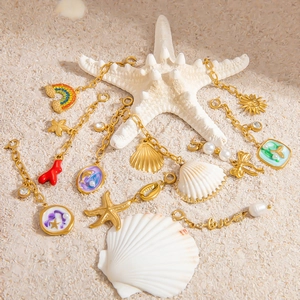 Starfish and seashell charms in 18K gold finish on a white sand beach background