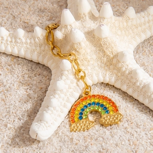 Rainbow charm with lobster clasp and gold chain on beach sand and white starfish