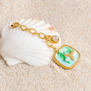 Detail of gold ocean tail pendant with colorful enamel and pearls on beach shell