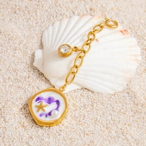 Detail of starfish charm and pearl pendant on a gold chain over seashells
