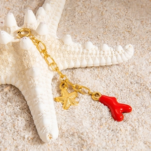 Detail of 18K gold starfish and red enamel coral pendant on a seaside beach setting