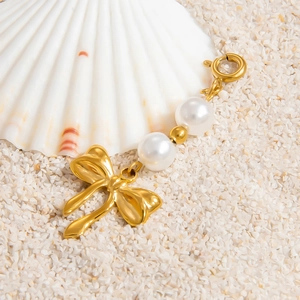 Golden bow pendant with white pearls and spring clasp on a beach shell background