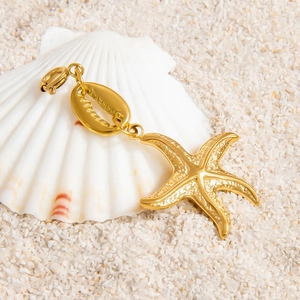 Detailed view of golden starfish and conch shell charms on white sand background