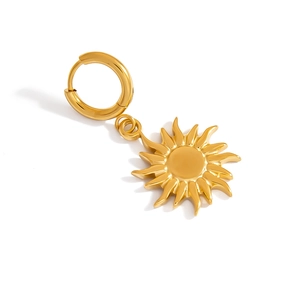 Macro view of golden sun pendant earring with polished radiant rays on white surface
