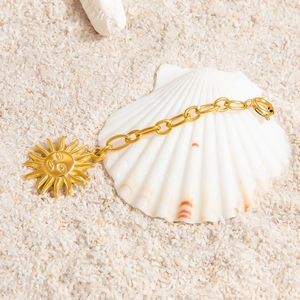 Detail of a gold-plated sun mask pendant on an oval link chain against white sand